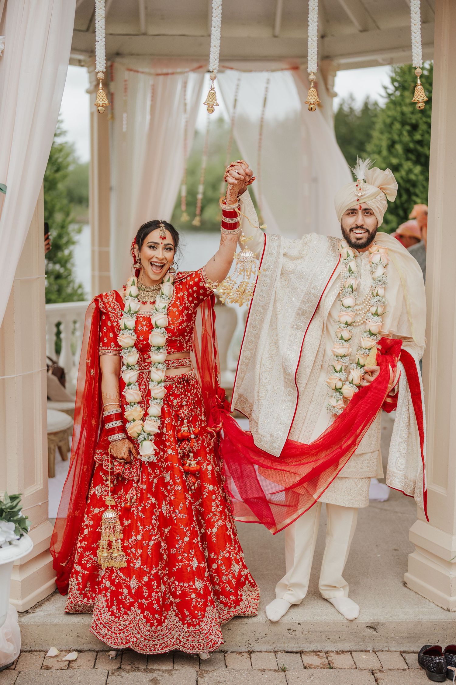 Happy Hindu couple holding hands and cheering joyfully after wedding ceremony, celebrating together in vibrant traditional attire in toronto