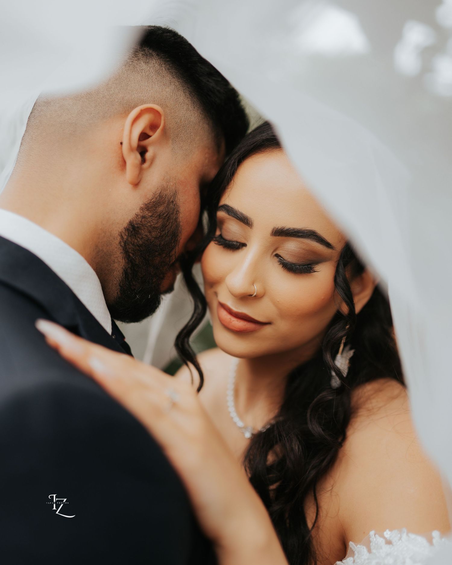 Intimate super close-up of Indian couple’s faces partially covered under a white wedding dress veil, capturing tender and romantic moment