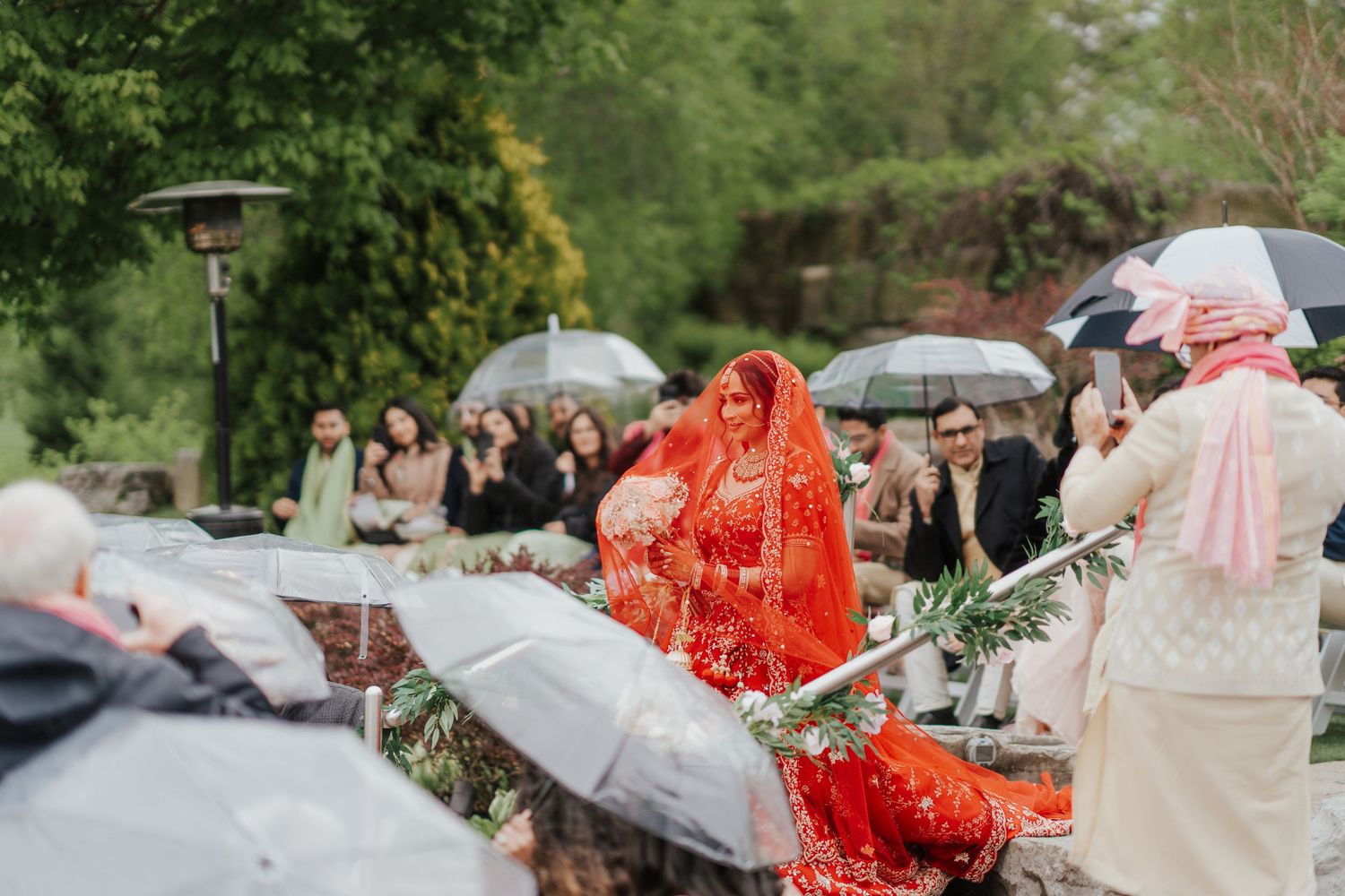 Beautiful Hindu bride walking gracefully to ceremony, holding vibrant flower bouquet with delicate veil draped over her head in toronto