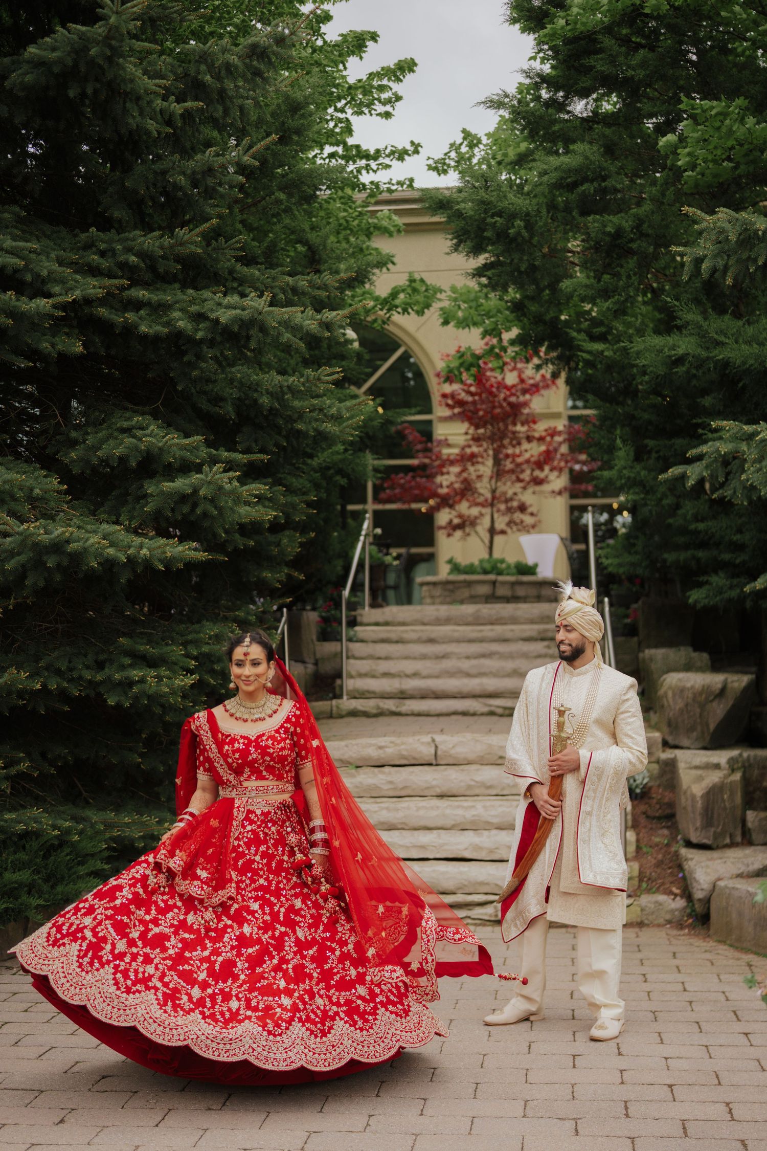 Elegant Indian bride twirling gracefully in traditional wedding dress during scenic outdoor photoshoot, capturing motion and cultural beauty