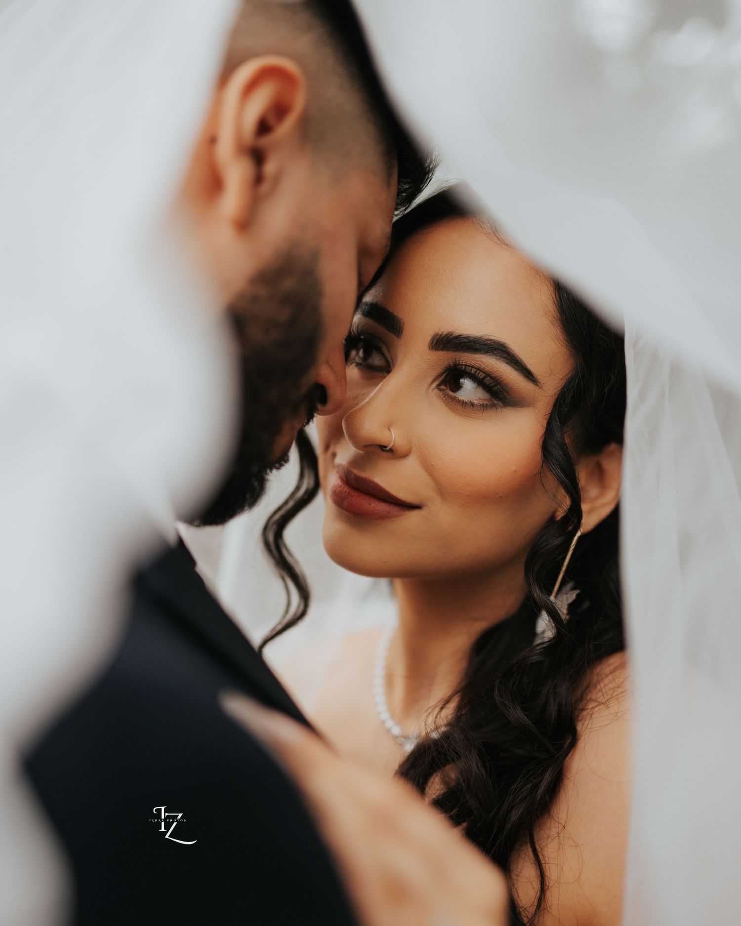 Intimate super close-up of Indian couple’s faces partially covered under a white wedding dress veil, capturing tender and romantic moment