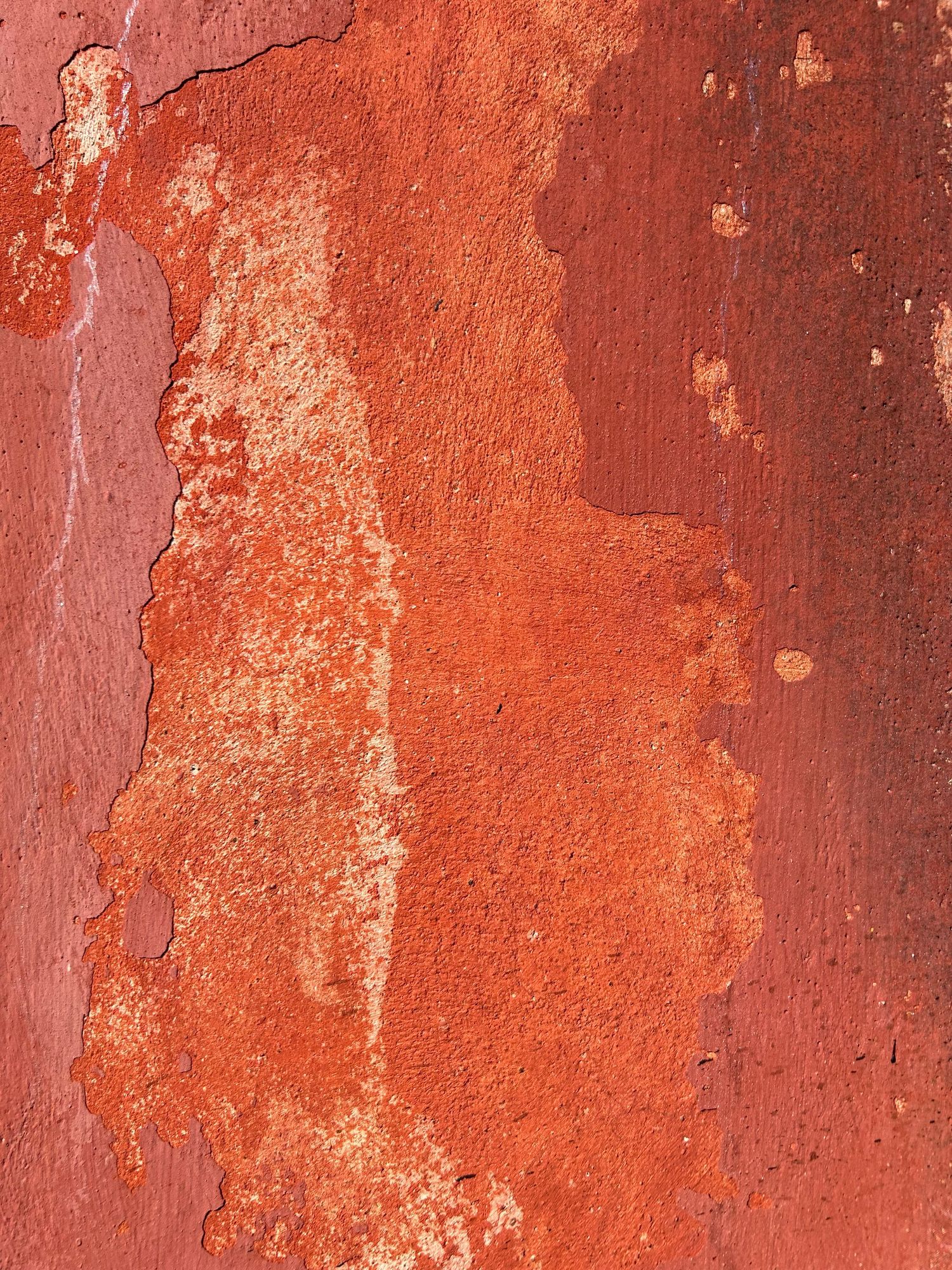 Distressed red wall surface showing layers of peeling paint and rustic texture.