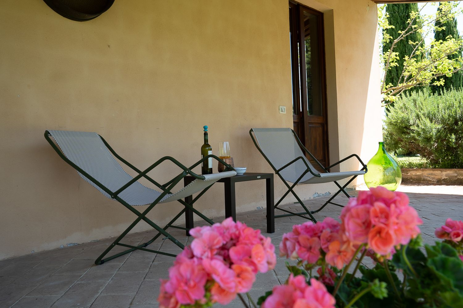Rustic veranda with folding chairs and pink flowering plants.