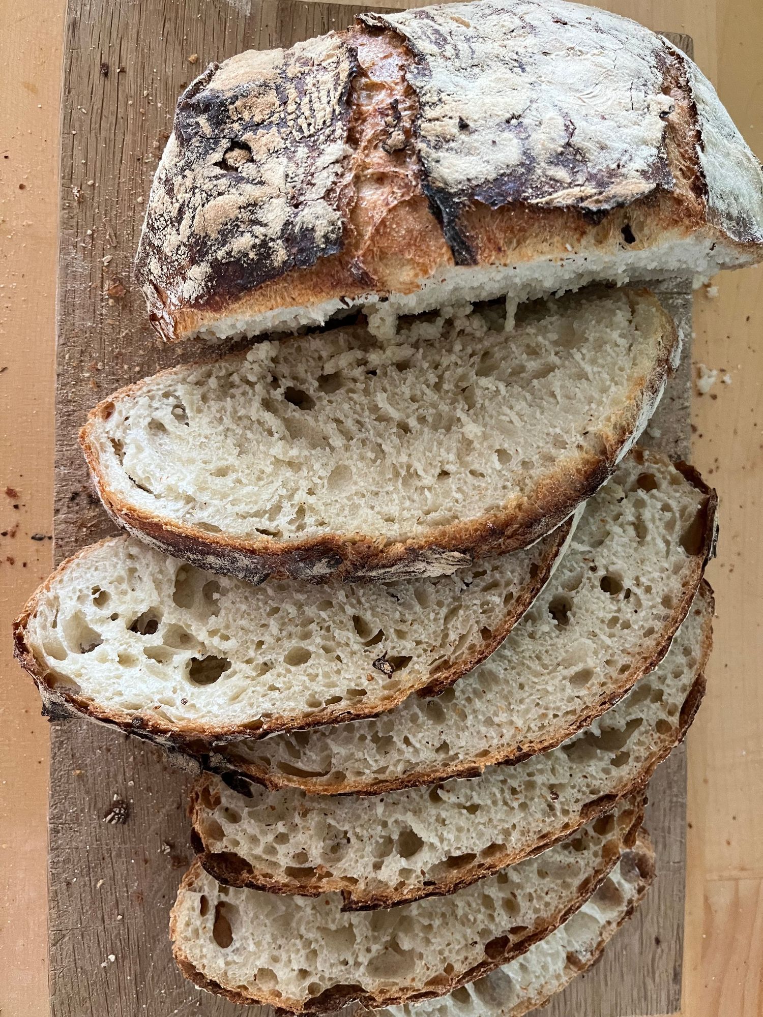 Sliced artisanal sourdough bread with a rustic crust and open crumb structure displayed on a wooden cutting board.
