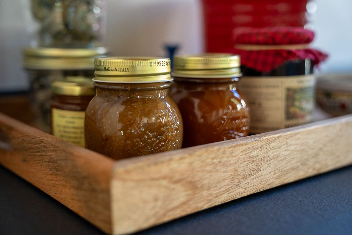 Homemade fruit preserves in glass mason jars with gold lids displayed on a rustic wooden serving tray.