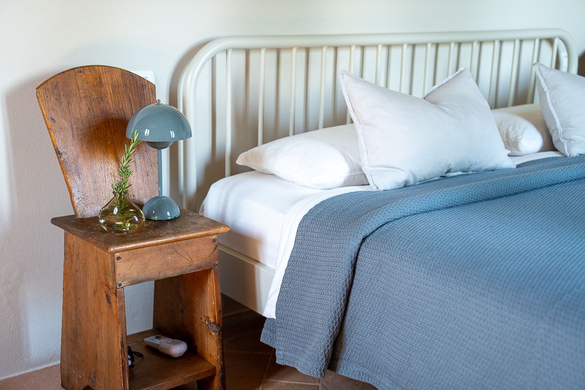 Cozy bedroom with blue waffle knit bedspread, white iron headboard, rustic wooden nightstand, and teal lamp.