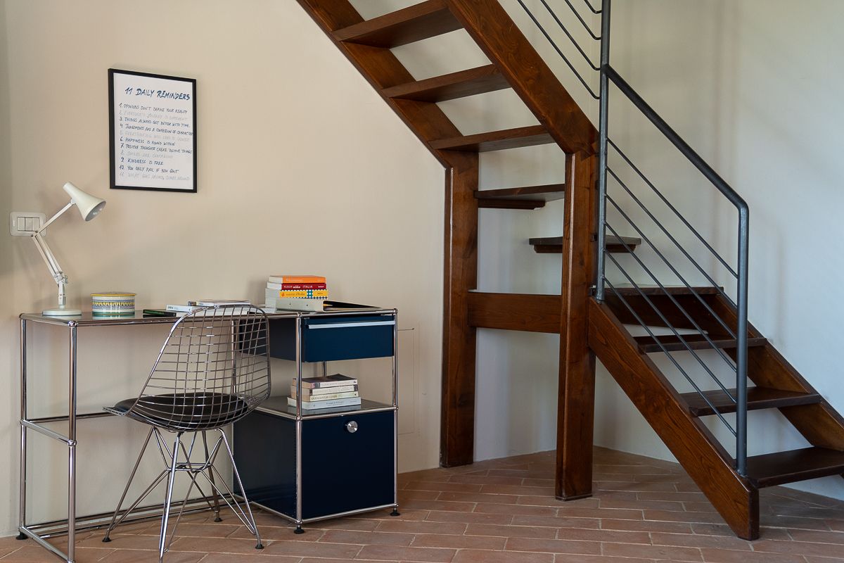 Modern home office nook under wooden staircase with Eames chair, USM desk, and metal cable railing.