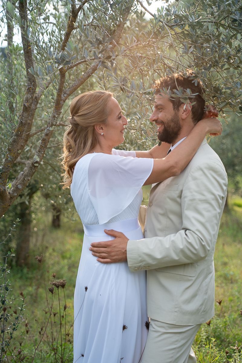 A couple embraces tenderly among olive trees in a romantic outdoor setting.
