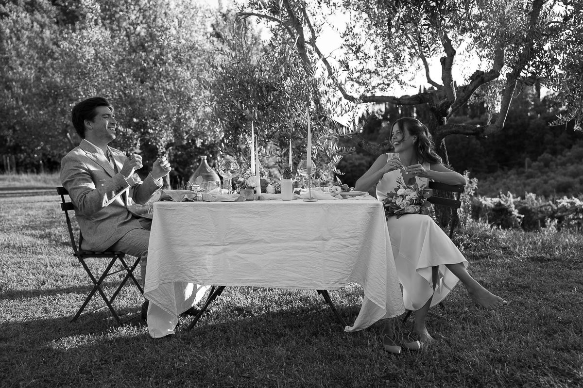 Black and white photo of a couple dining outdoors at a candlelit table set on a lush garden lawn.
