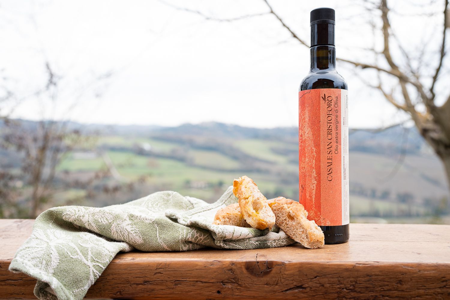 Olive Oil bottles and rustic bread displayed with countryside view in background.