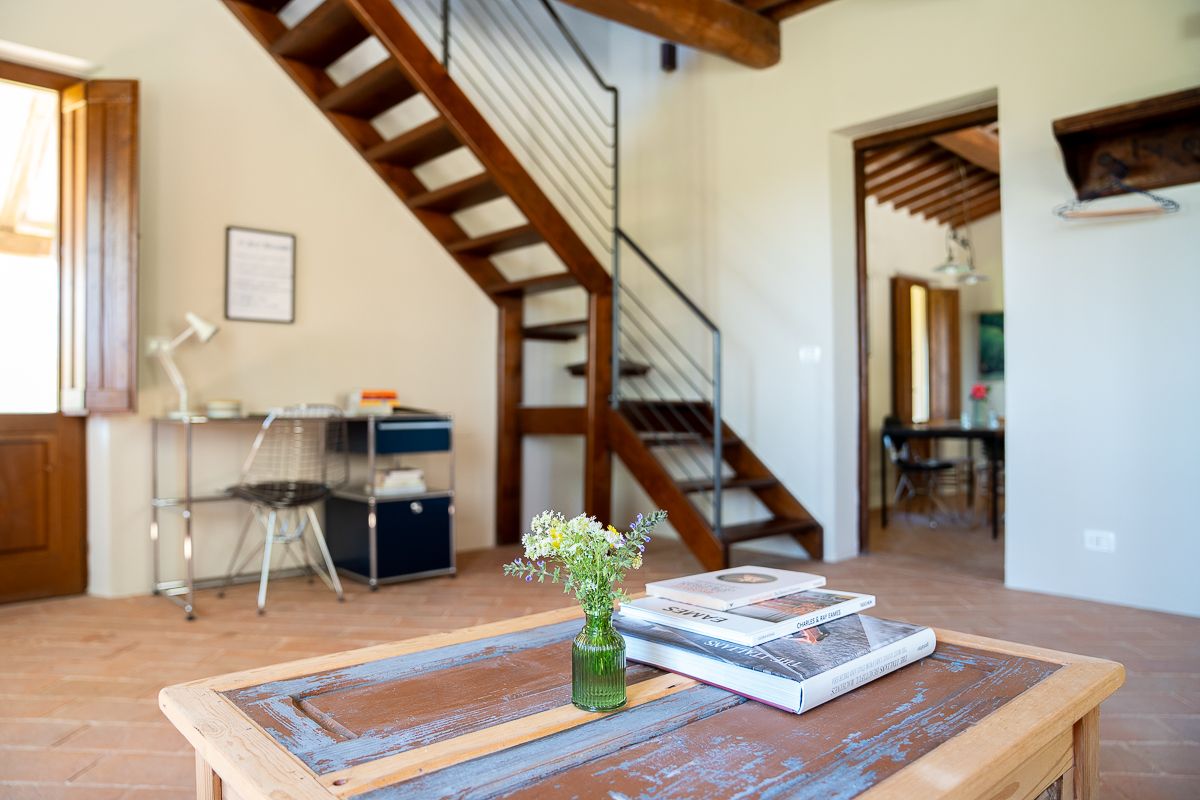 Rustic living room with wooden coffee table, wildflowers, staircase, and desk in a Tuscan farmhouse.