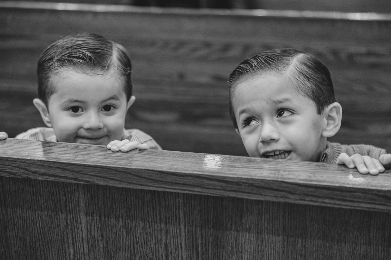 Playful black and white photo of children peeking over church pew.