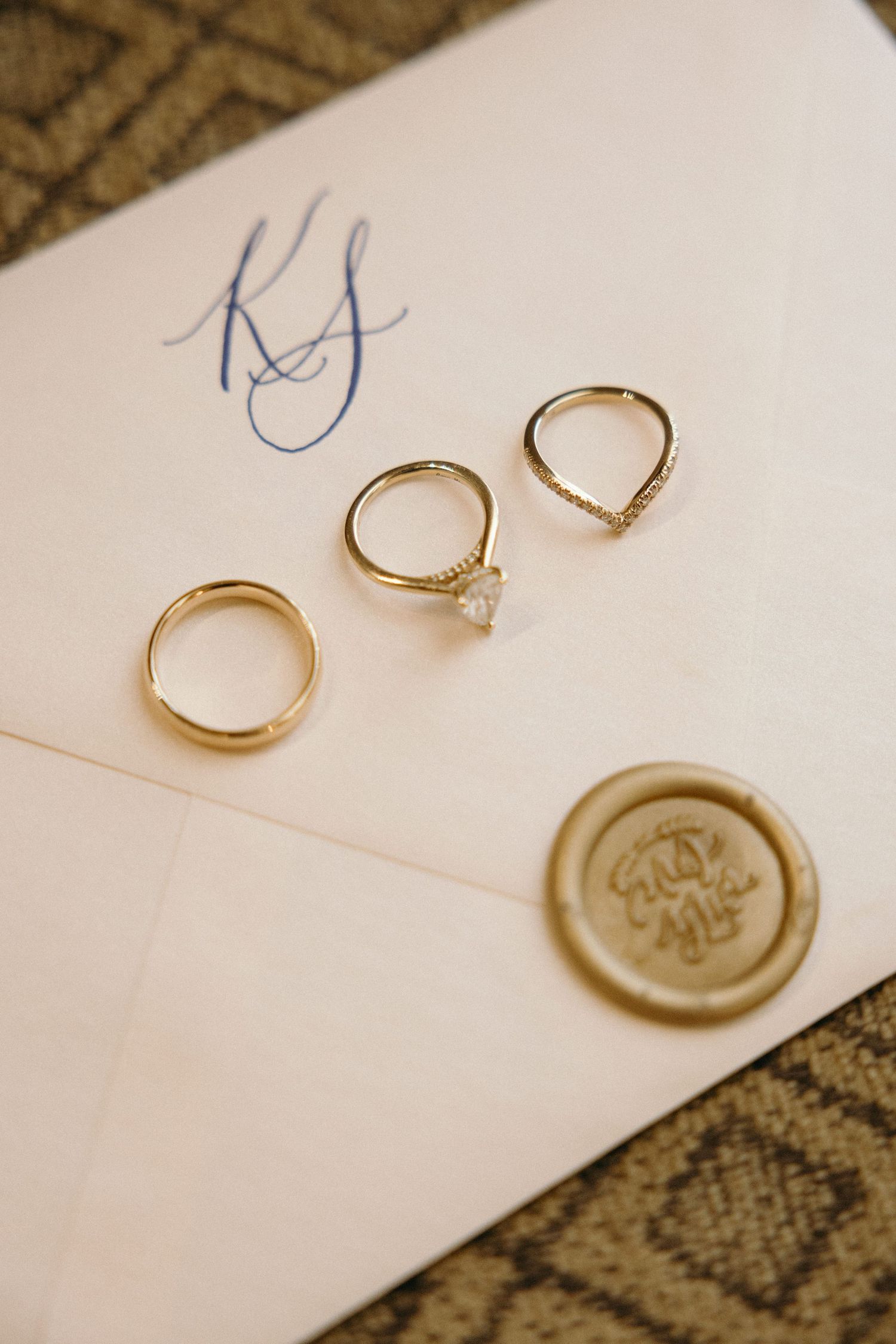 Three gold wedding rings and a wax seal arranged on paper with monogram initials.