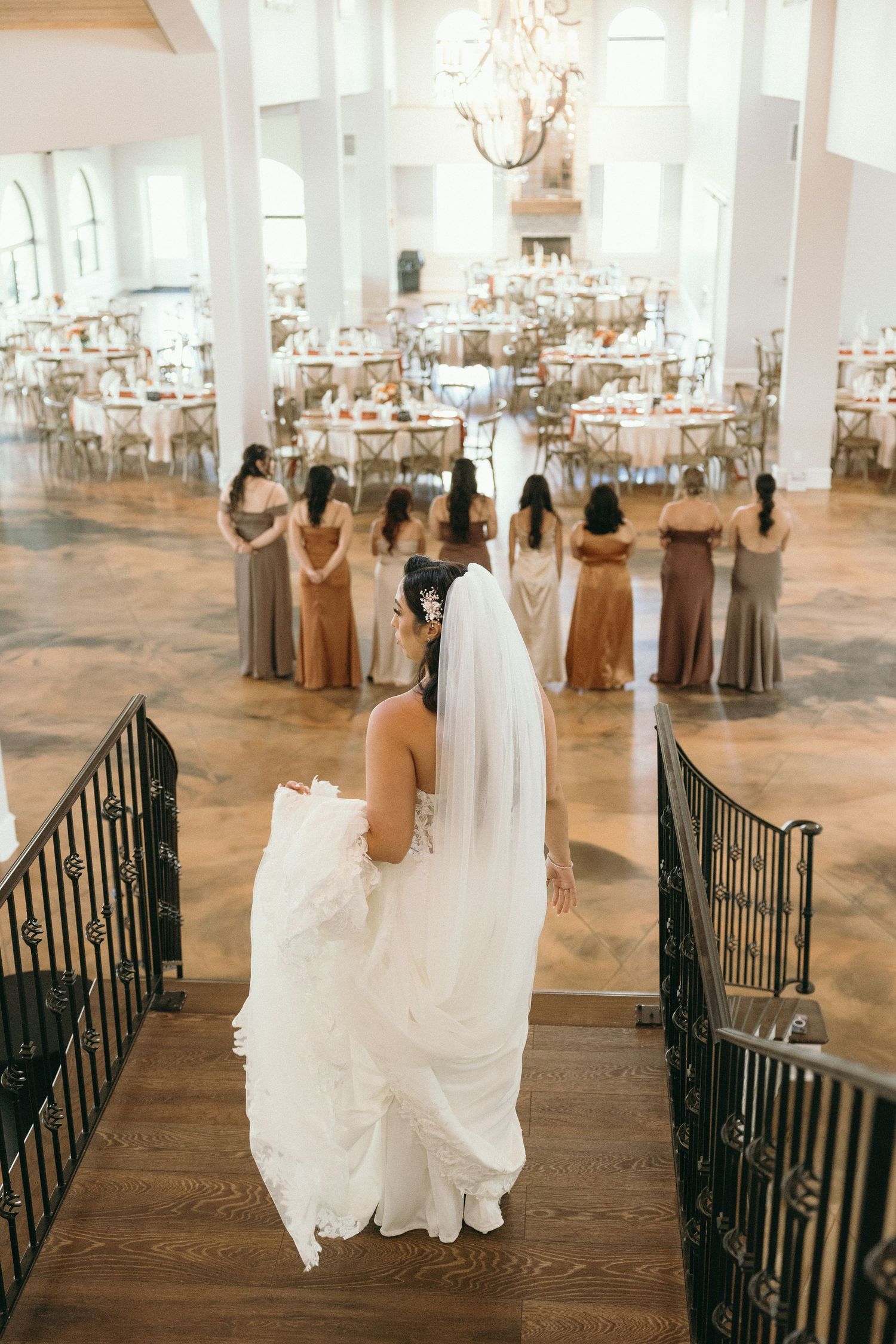 Bride and bridesmaids walking down elegant venue stairs in flowing dresses.