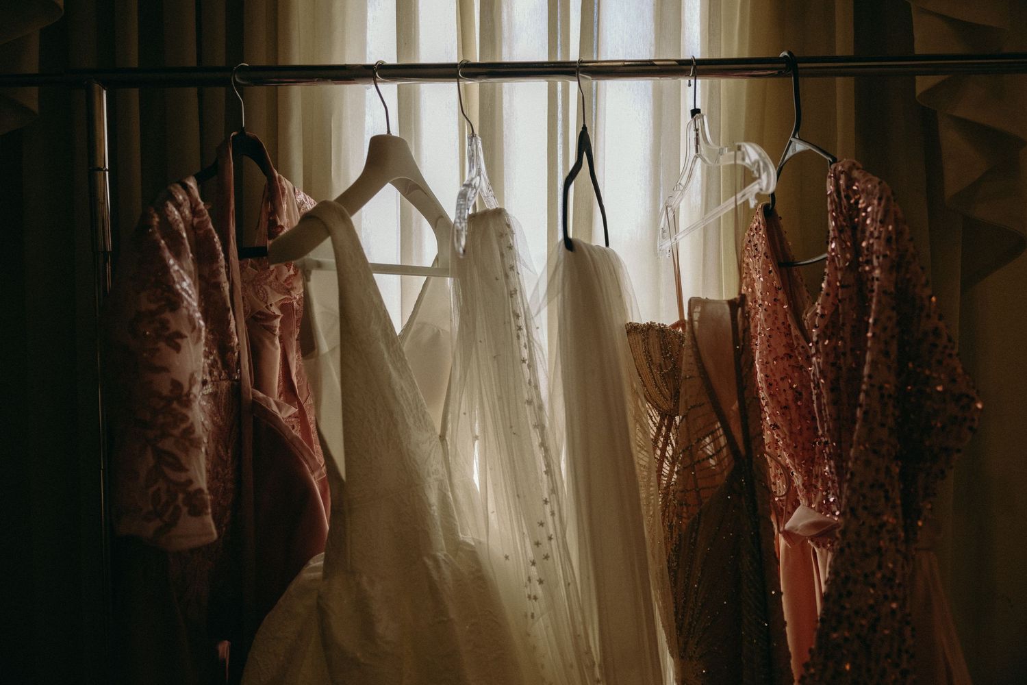 Sunlit window with sheer curtains and hanging burgundy bridesmaid dresses.