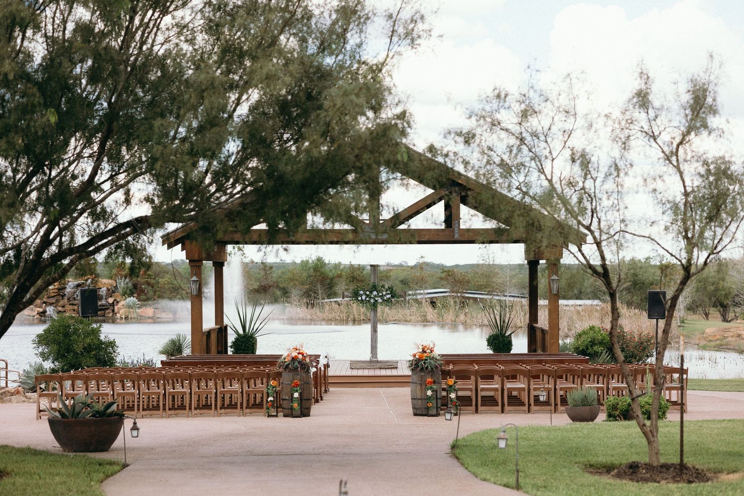 Wedding venue setup with wooden benches and rustic pavilion against natural landscape.