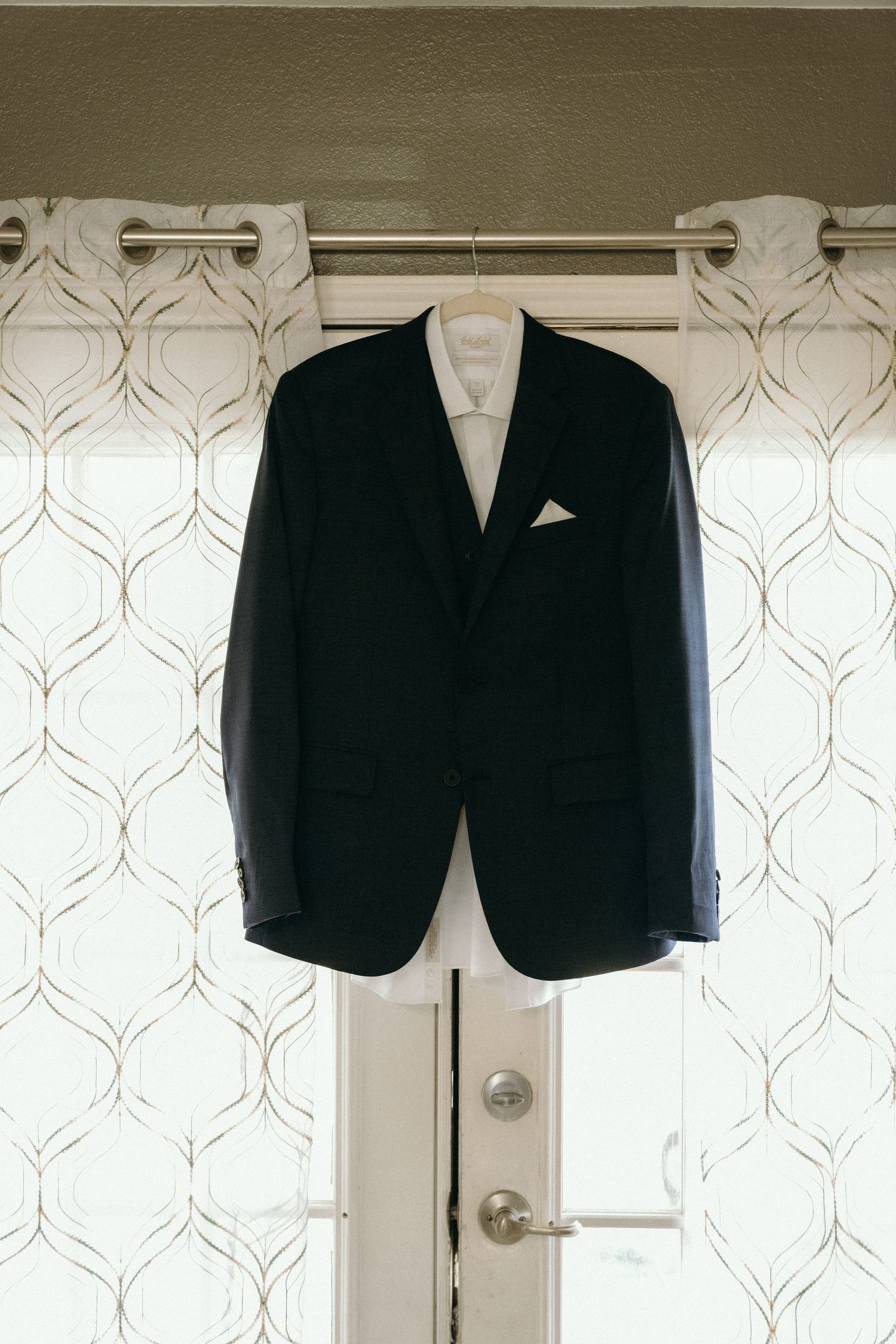 Black suit jackets hanging on white textured wall before wedding ceremony.