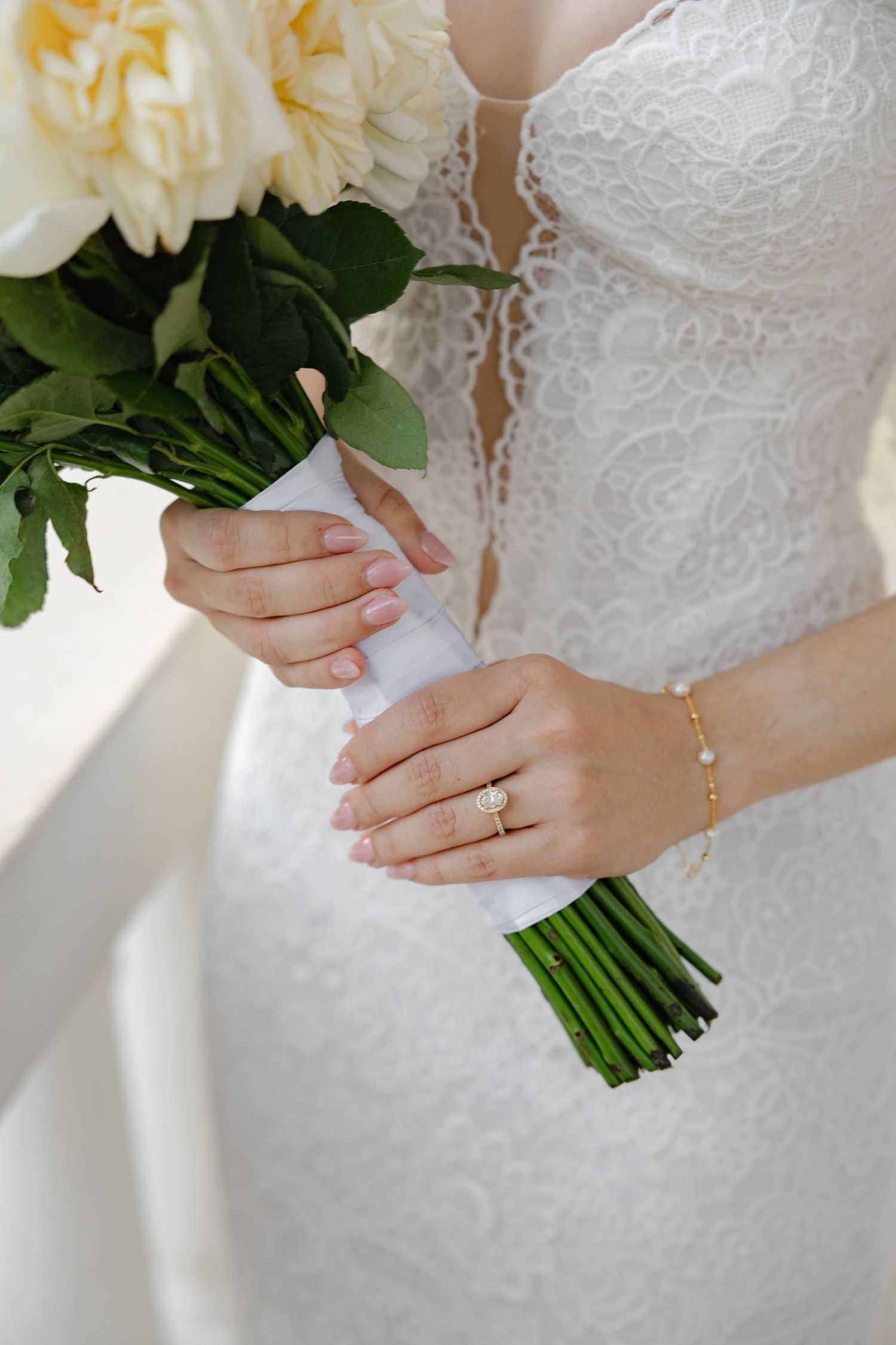 Close-up of white bridal bouquet with cream roses held by hands in lace dress.