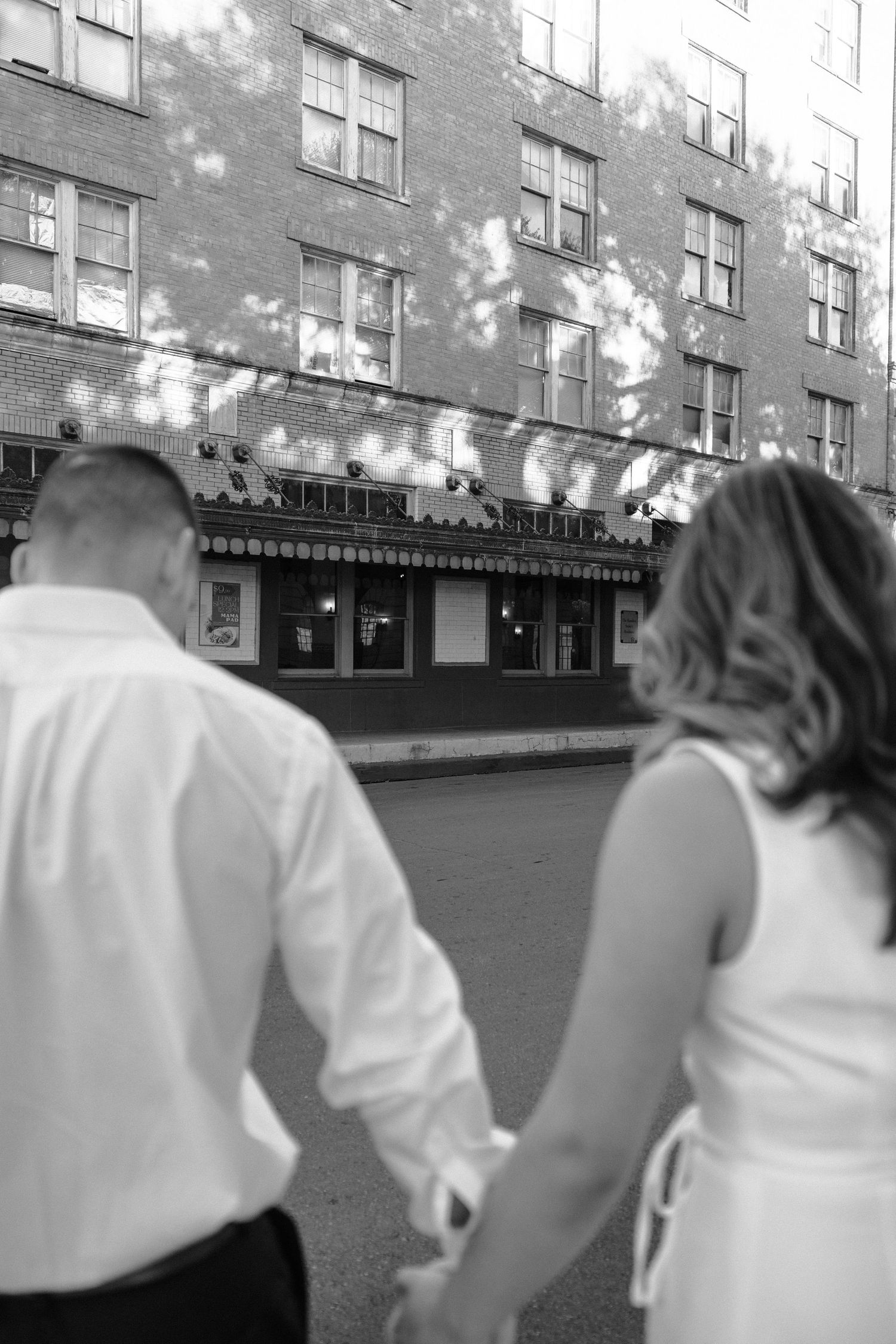 Black and white image of people walking past brick buildings on a city street.