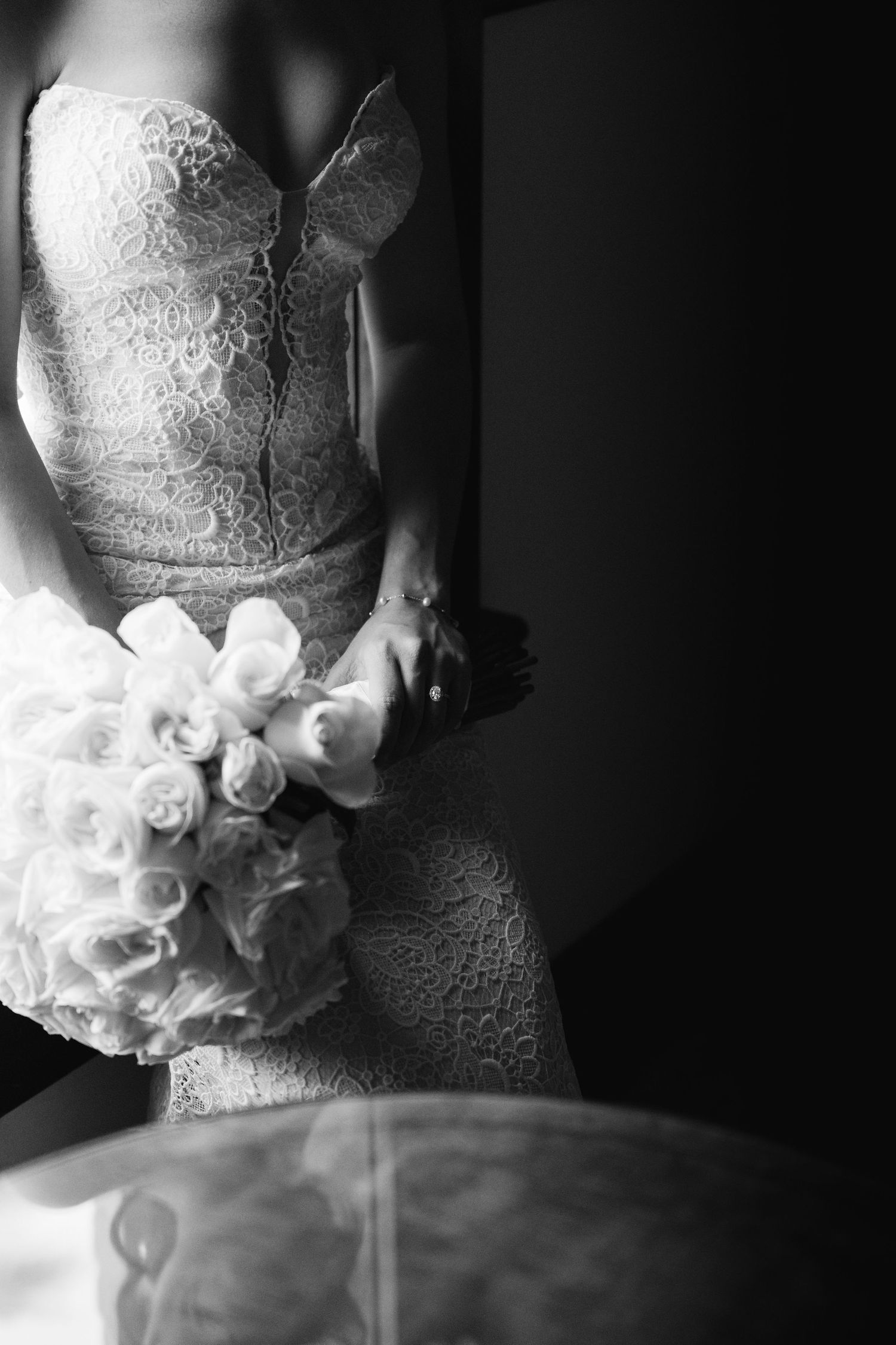 Elegant lace wedding dress detail in dramatic black and white lighting.