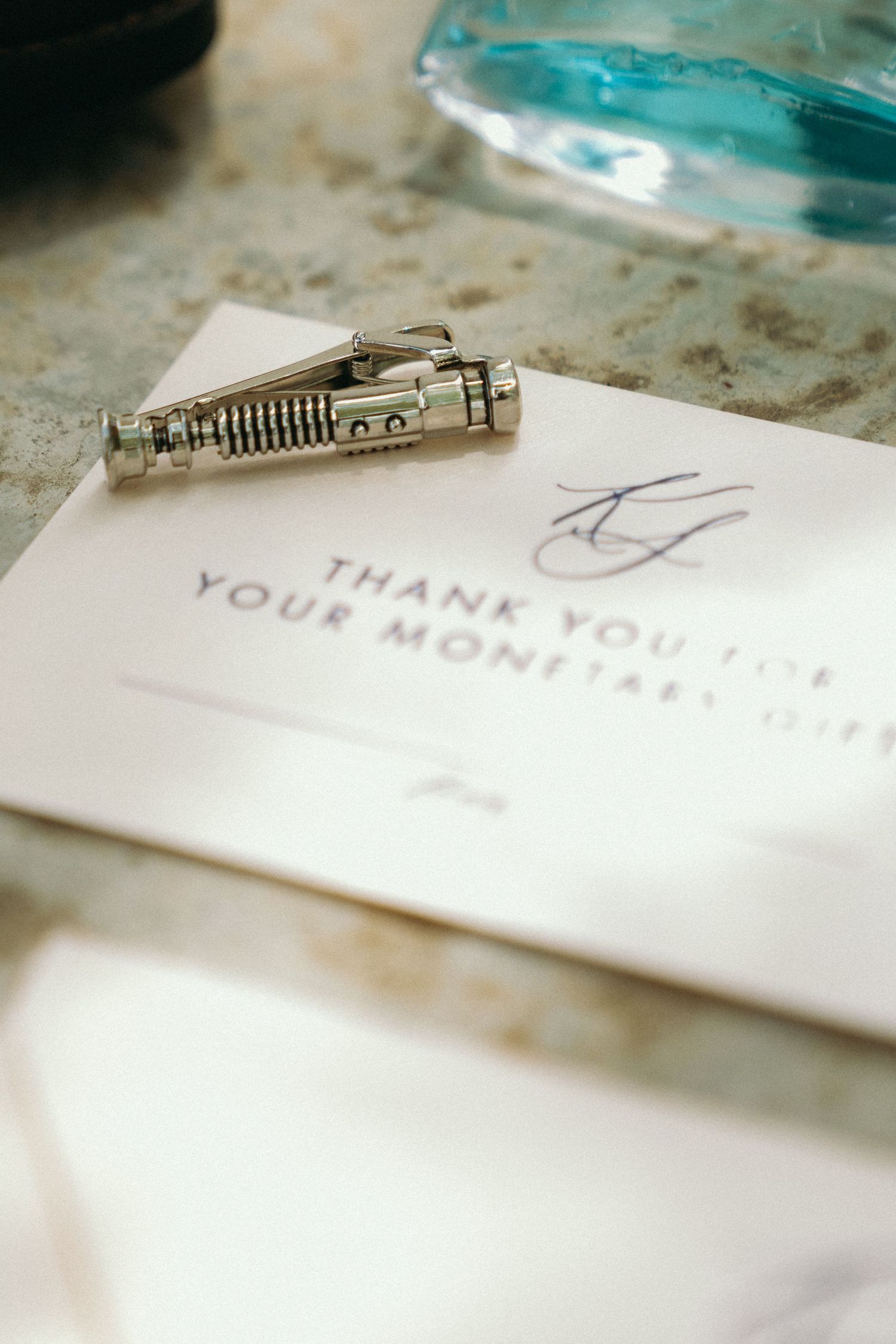 A handwritten thank you note being written with a turquoise pen on white paper.