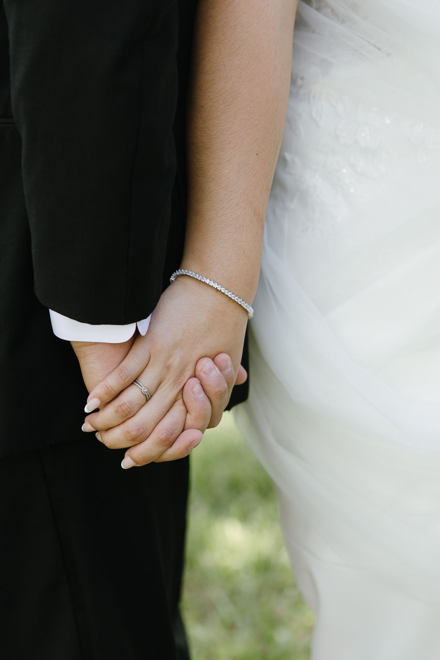 Detail shots of bride and groom holding hands with wedding rings and bracelets.