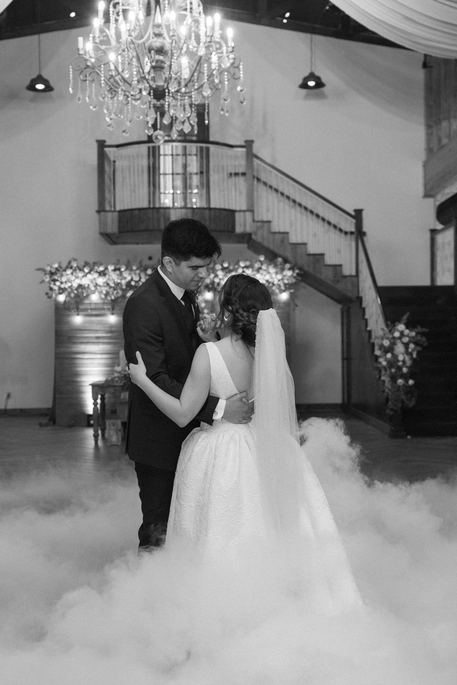 Wedding couple dancing in fog on a dance floor under crystal chandeliers.