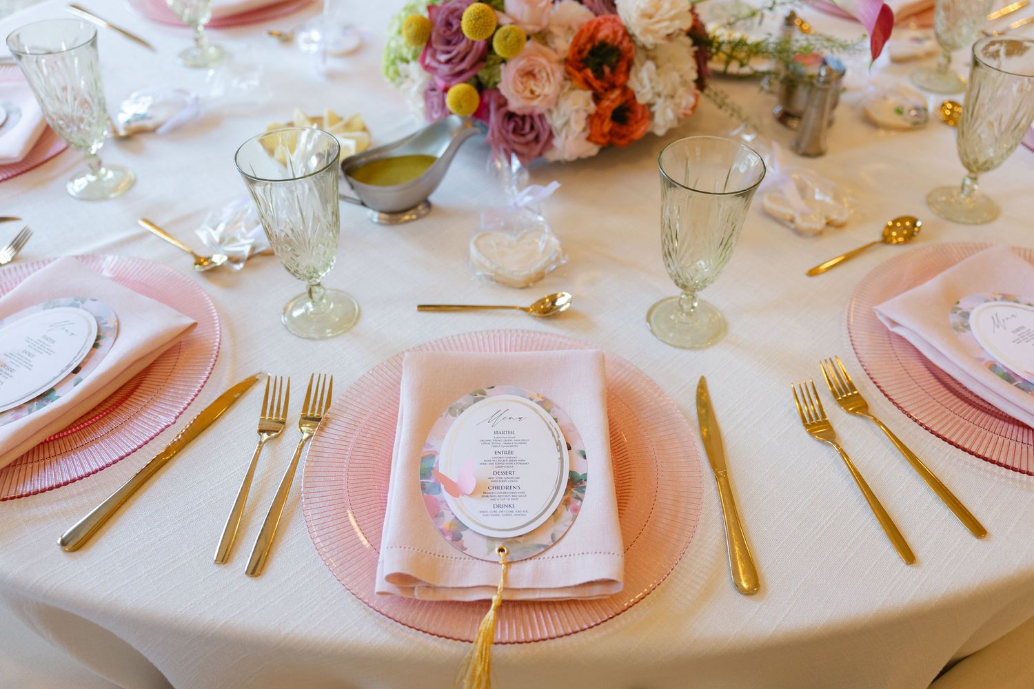 Wedding reception table with pink and gold place settings and floral centerpieces.