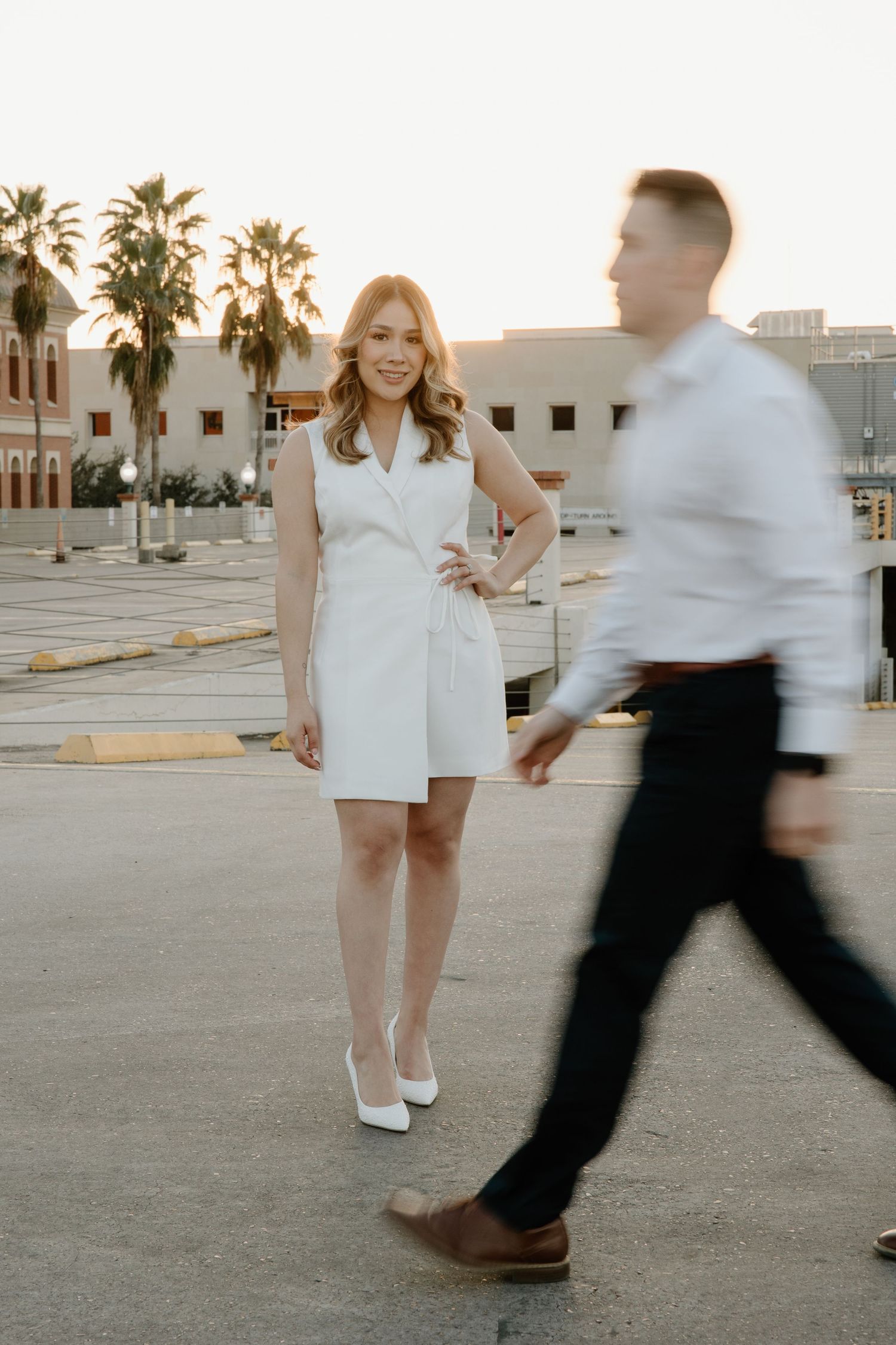 Couple in white and black outfits dancing playfully in a sunlit outdoor setting.