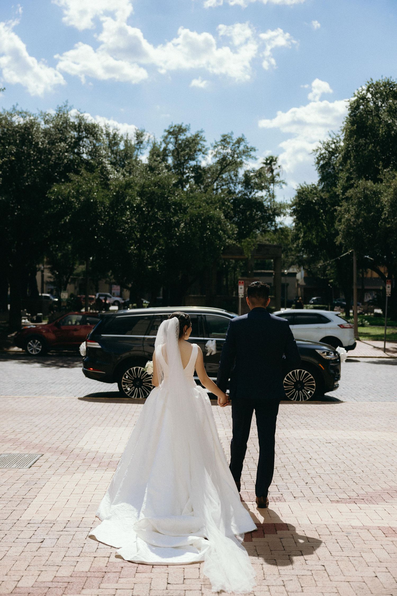 A couple walking together on a sunny day in a parking lot, with the bride wearing a flowing white wedding dress.