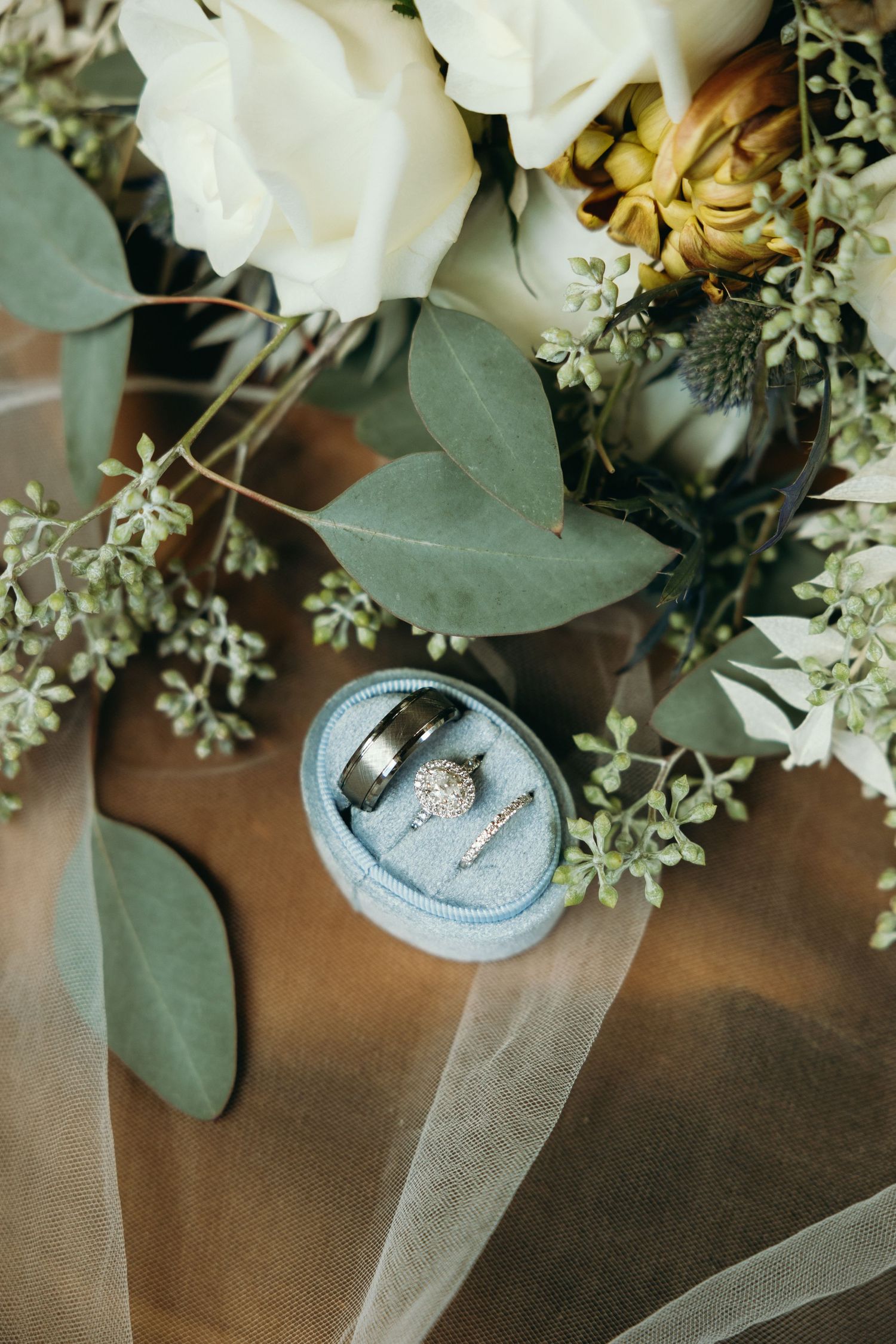 Wedding rings nestled among white roses and eucalyptus leaves in an elegant floral arrangement.