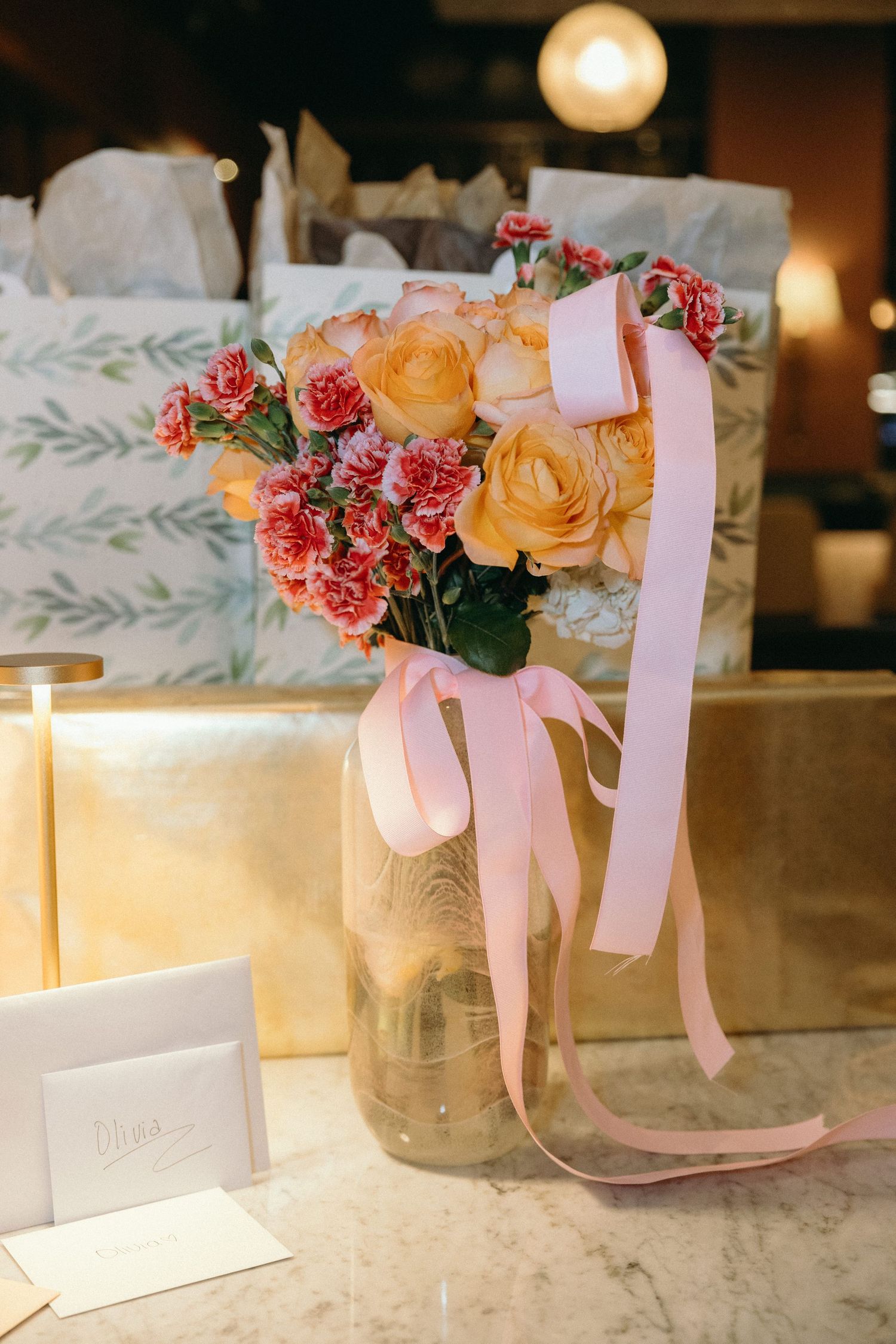 Mason jars with pink ribbons and fresh flowers arranged on a marble surface with place cards.