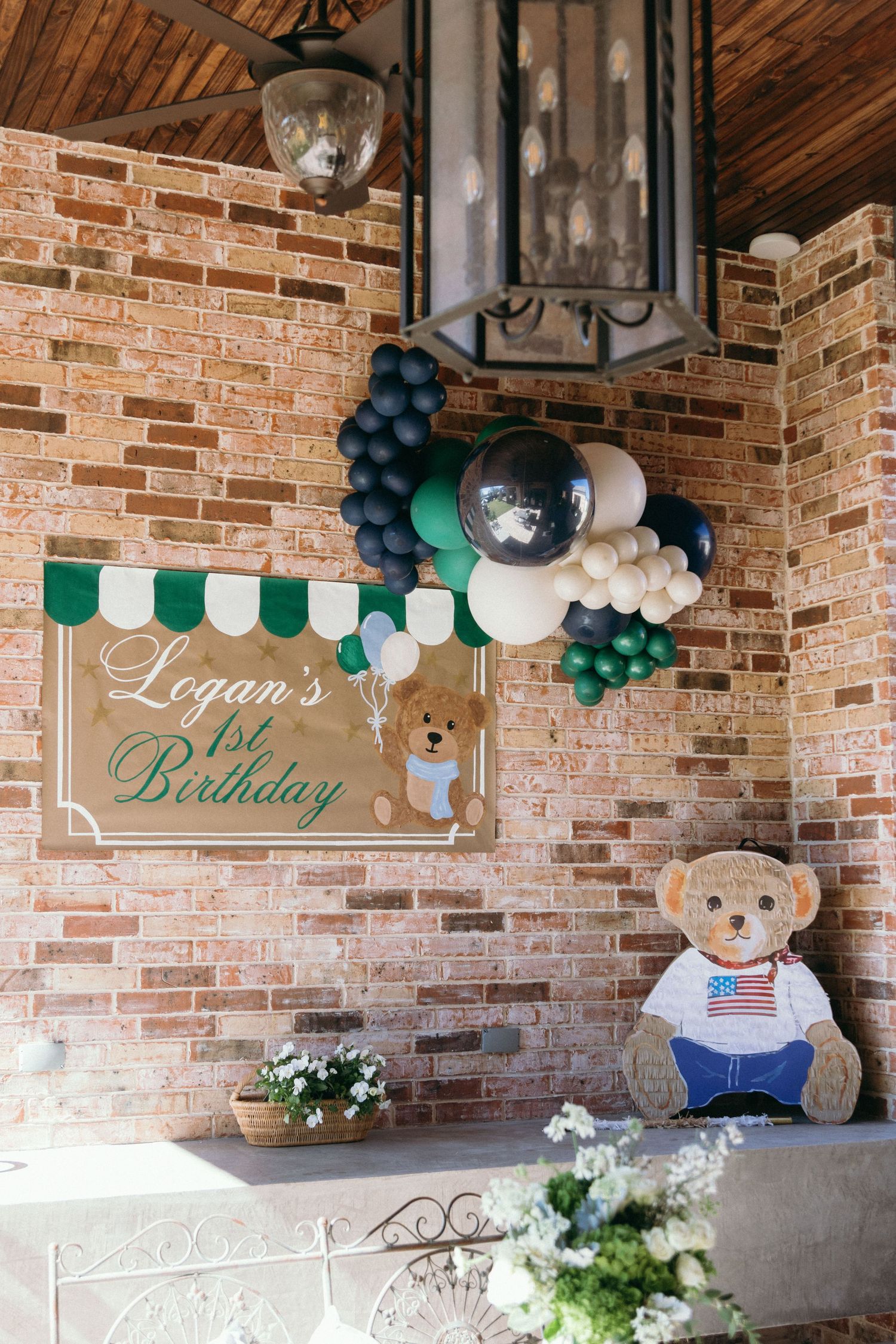 Birthday party decoration with green and navy balloons against a brick wall backdrop.