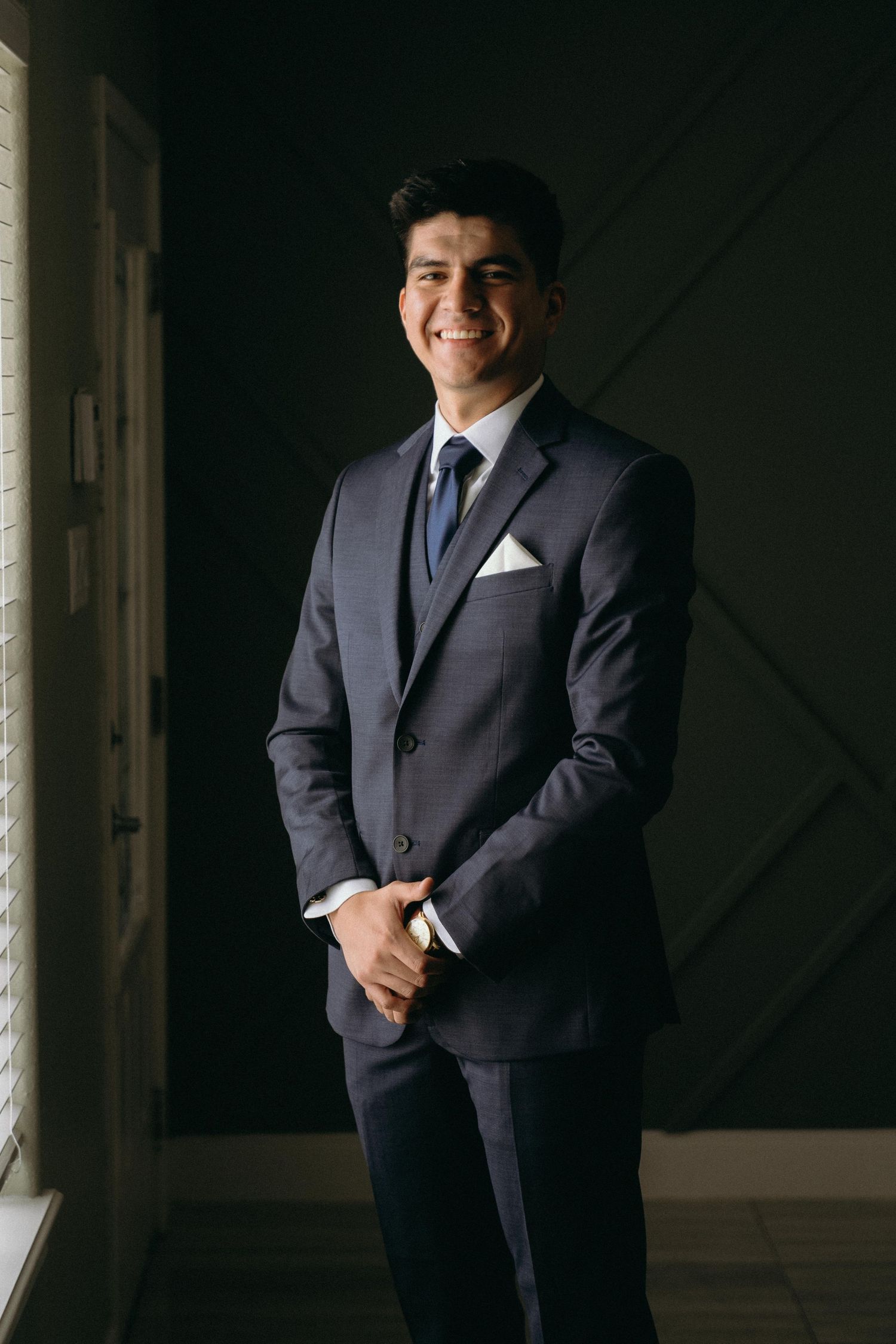 Groom in classic navy suit poses against dark background in professional portraits.