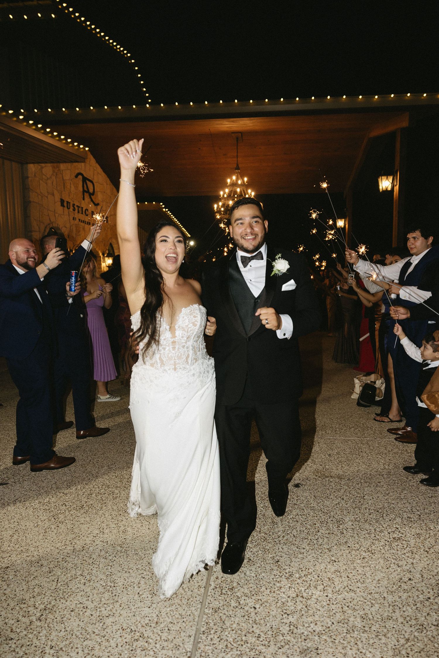 A celebratory exit as newlyweds walk through guests under string lights in an indoor venue.