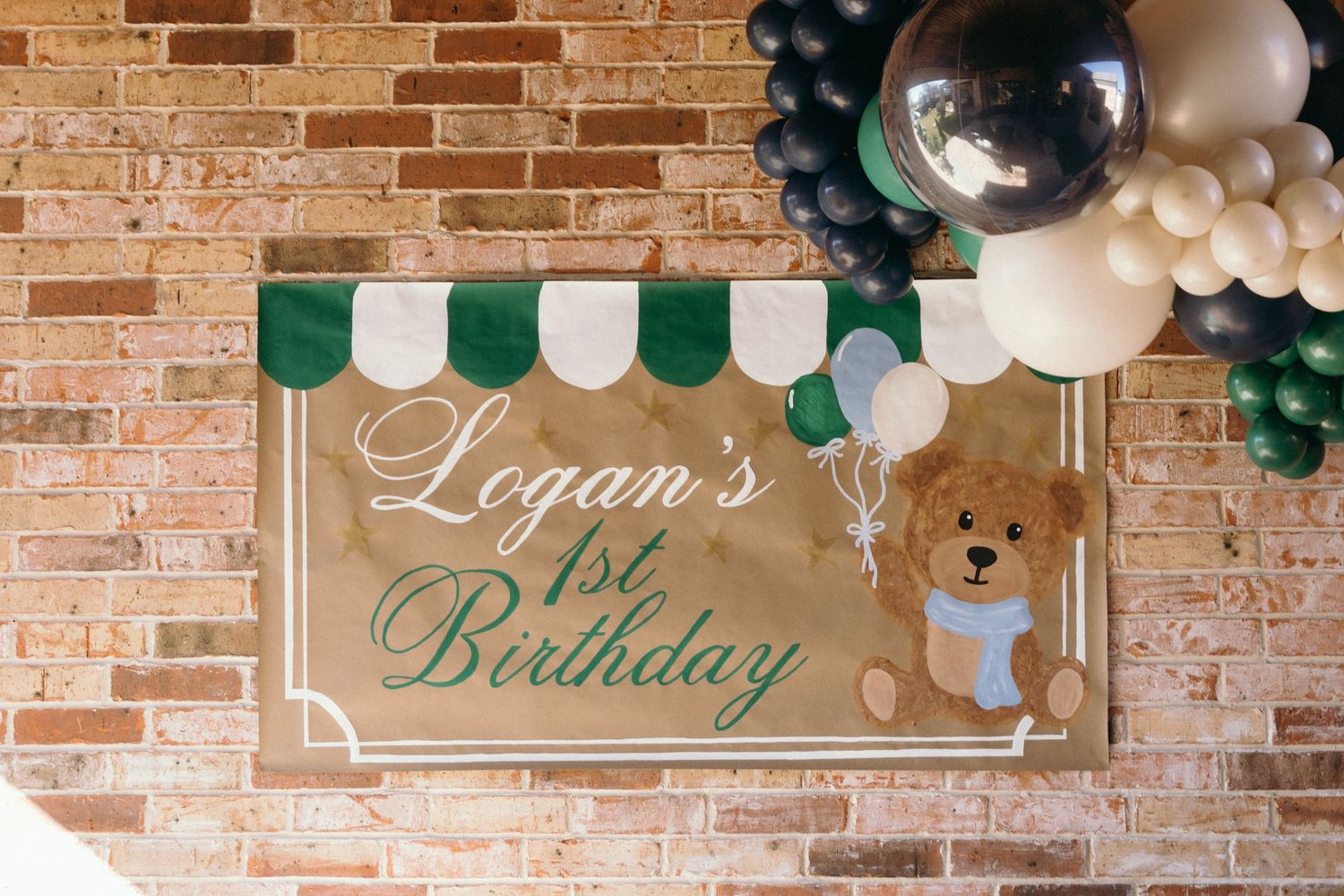 Birthday celebration setup with green and white balloon arrangements against a brick wall.