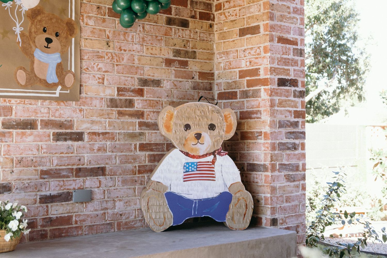Rustic brick wall decorated with balloon garlands and teddy bear themed party elements.