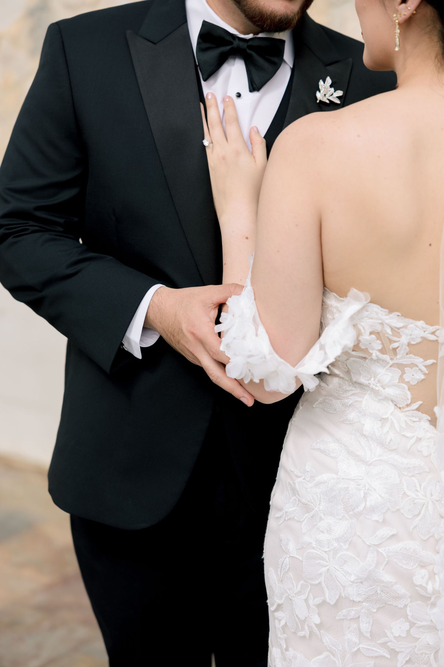 Bride and groom embracing, groom in black tuxedo with bow tie, bride in white lace backless wedding gown.