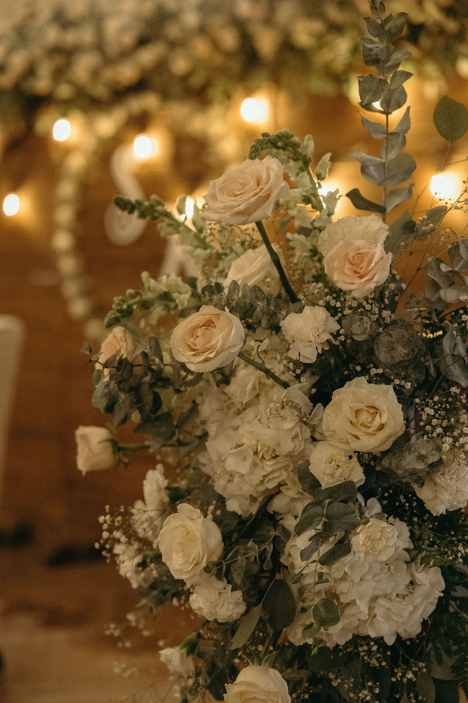 Romantic floral centerpiece with white roses and greenery under warm lighting.