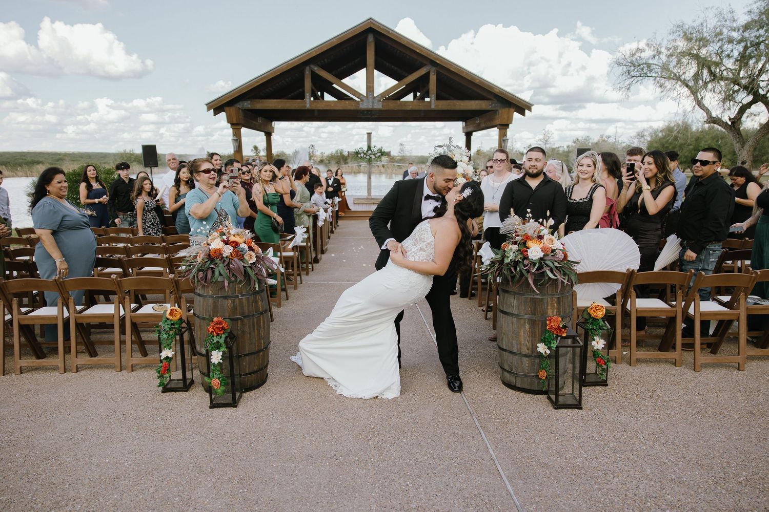 Panoramic view of wedding ceremony under wooden pavilion with guests seated on benches.