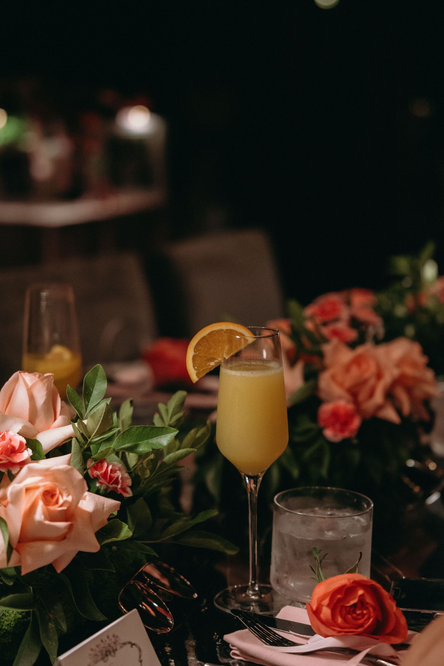 Elegant table setting with orange juice cocktails, roses, and candlelight at an evening event.