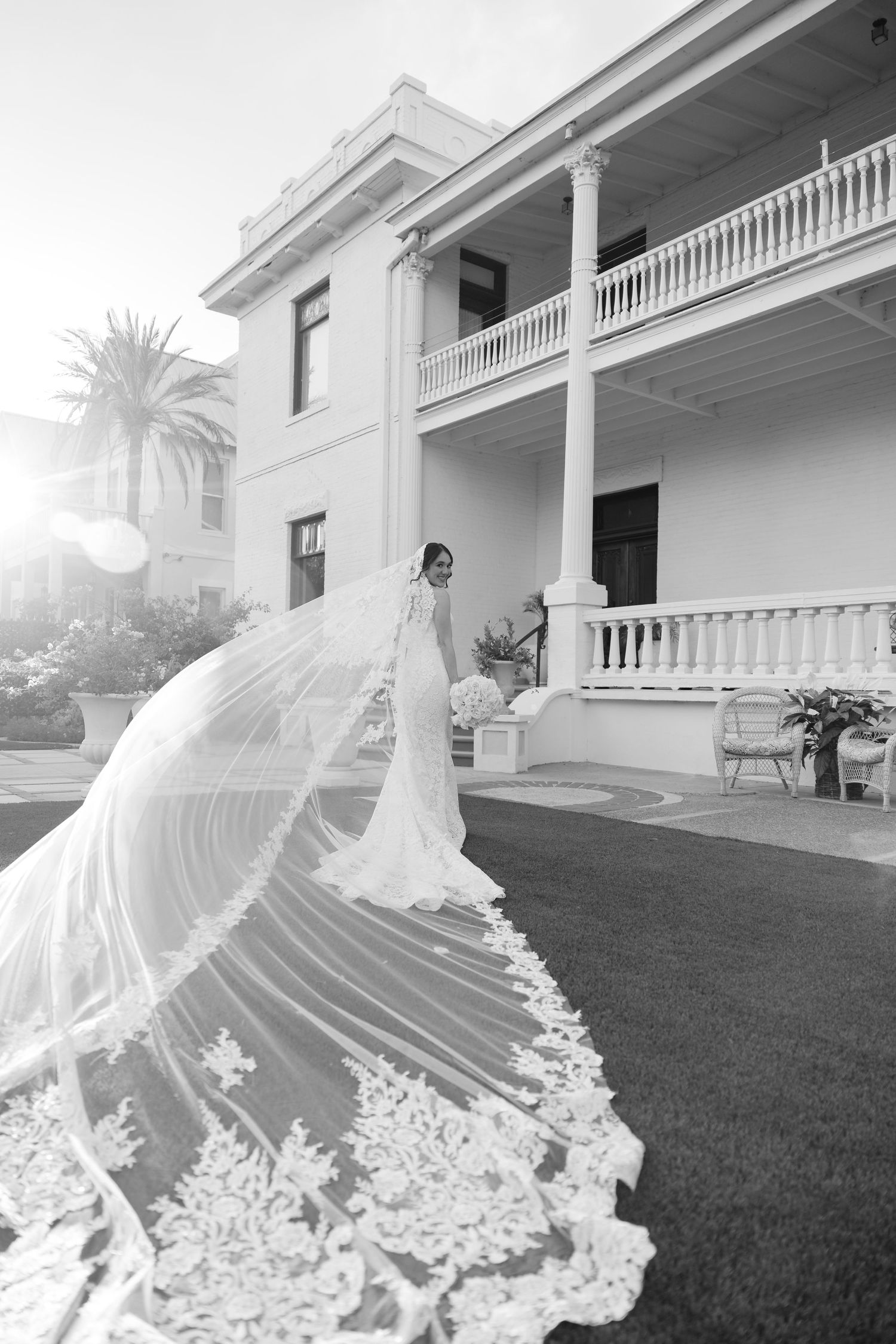 Wedding dress train flowing across green lawn in front of white colonial mansion.
