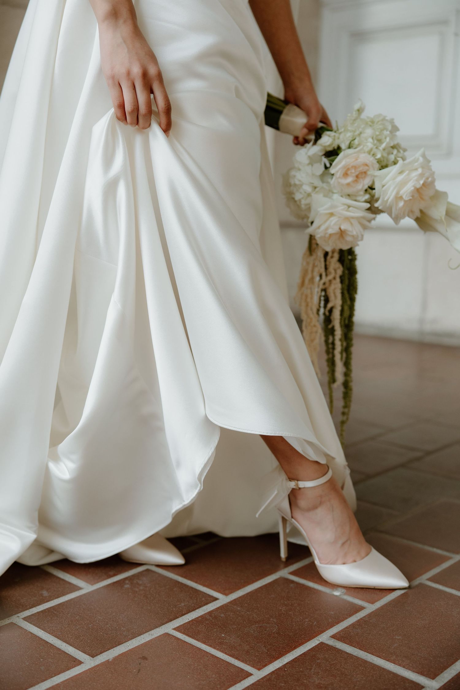 Detail shots of a white wedding dress hem and shoes on terracotta tile flooring.