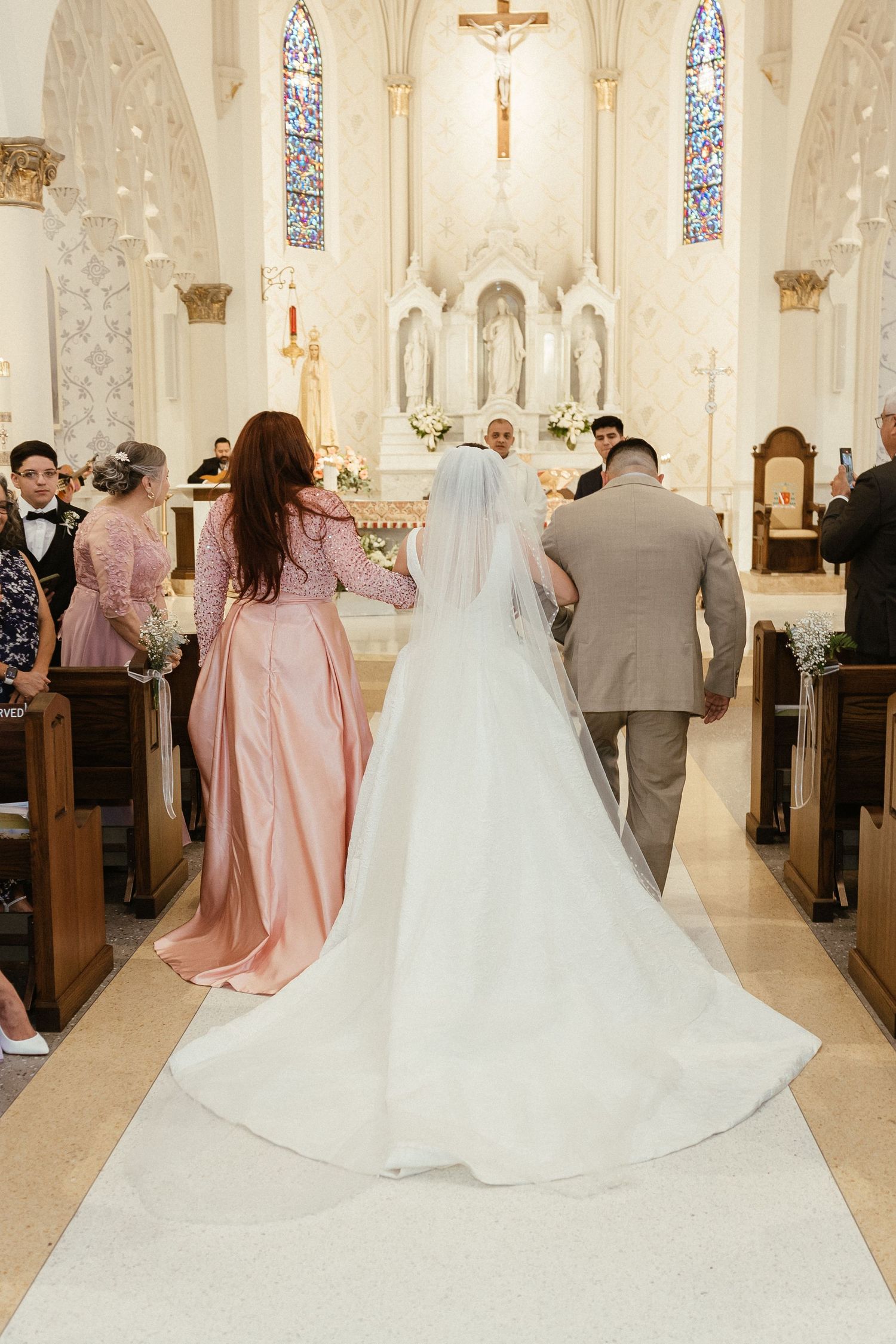 Wedding ceremony in a church with bridesmaids in pink dresses and bride in white gown.