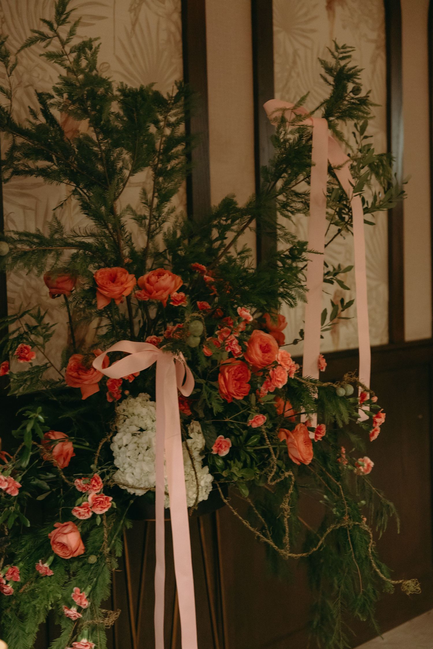 Floral arrangement with coral roses and greenery adorning a decorative wall display.