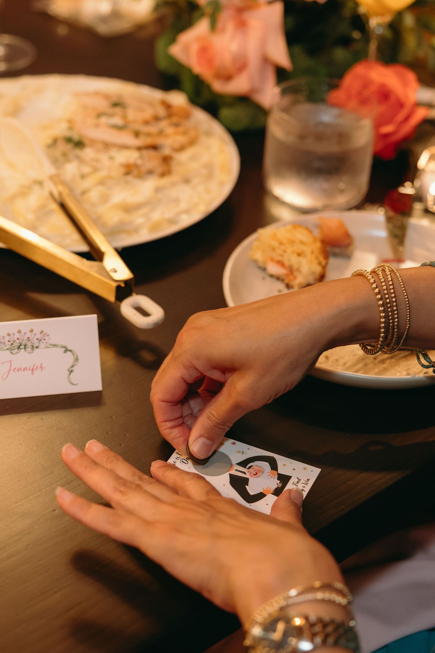 Hands holding cards and plates at a decorated table setting with roses.