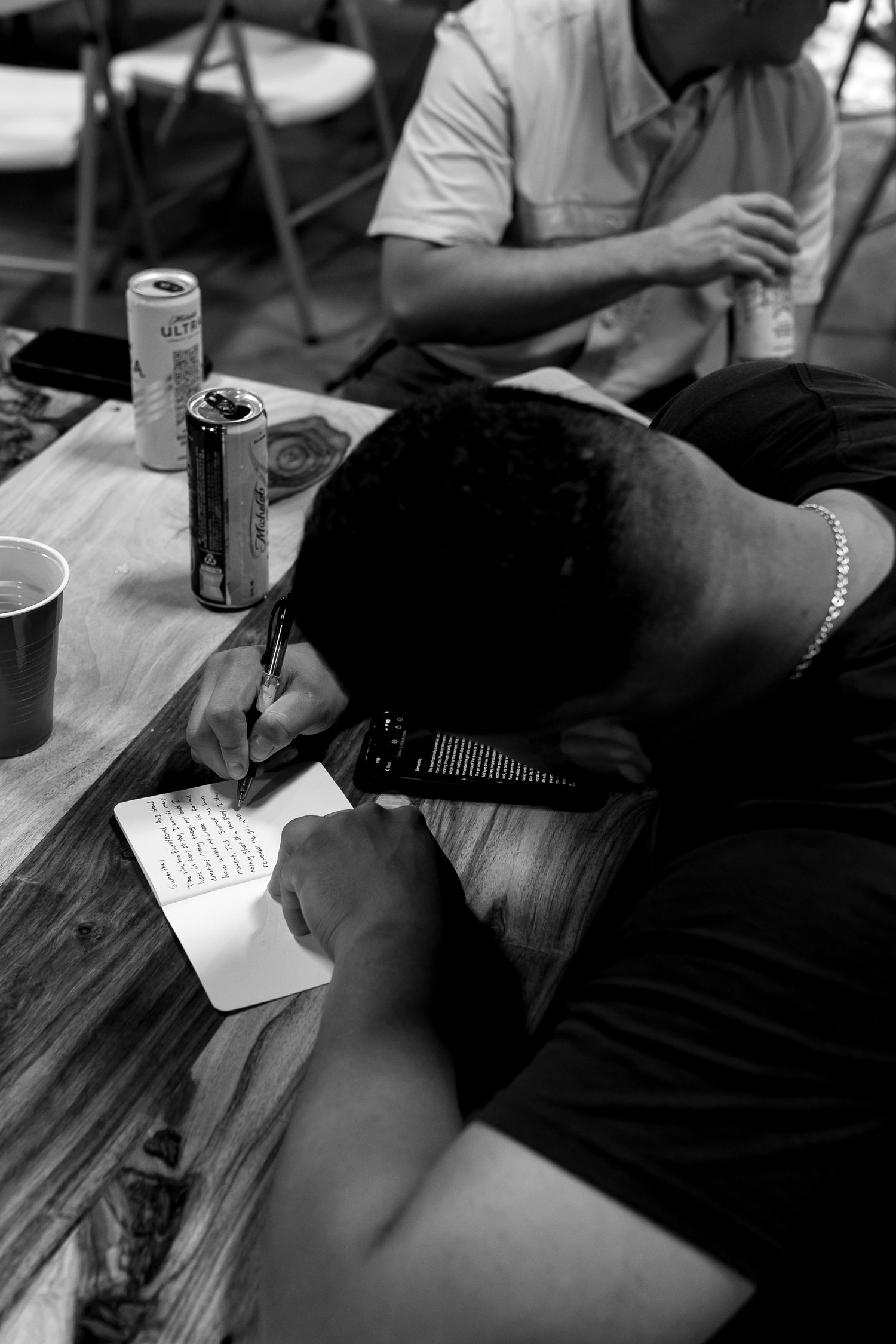 Wedding guests writing messages at reception table with drinks and paper.