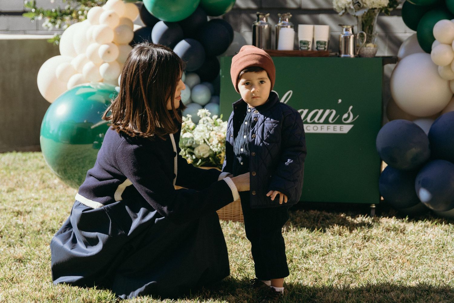 Outdoor celebration scene with green and navy balloon decorations on grass.
