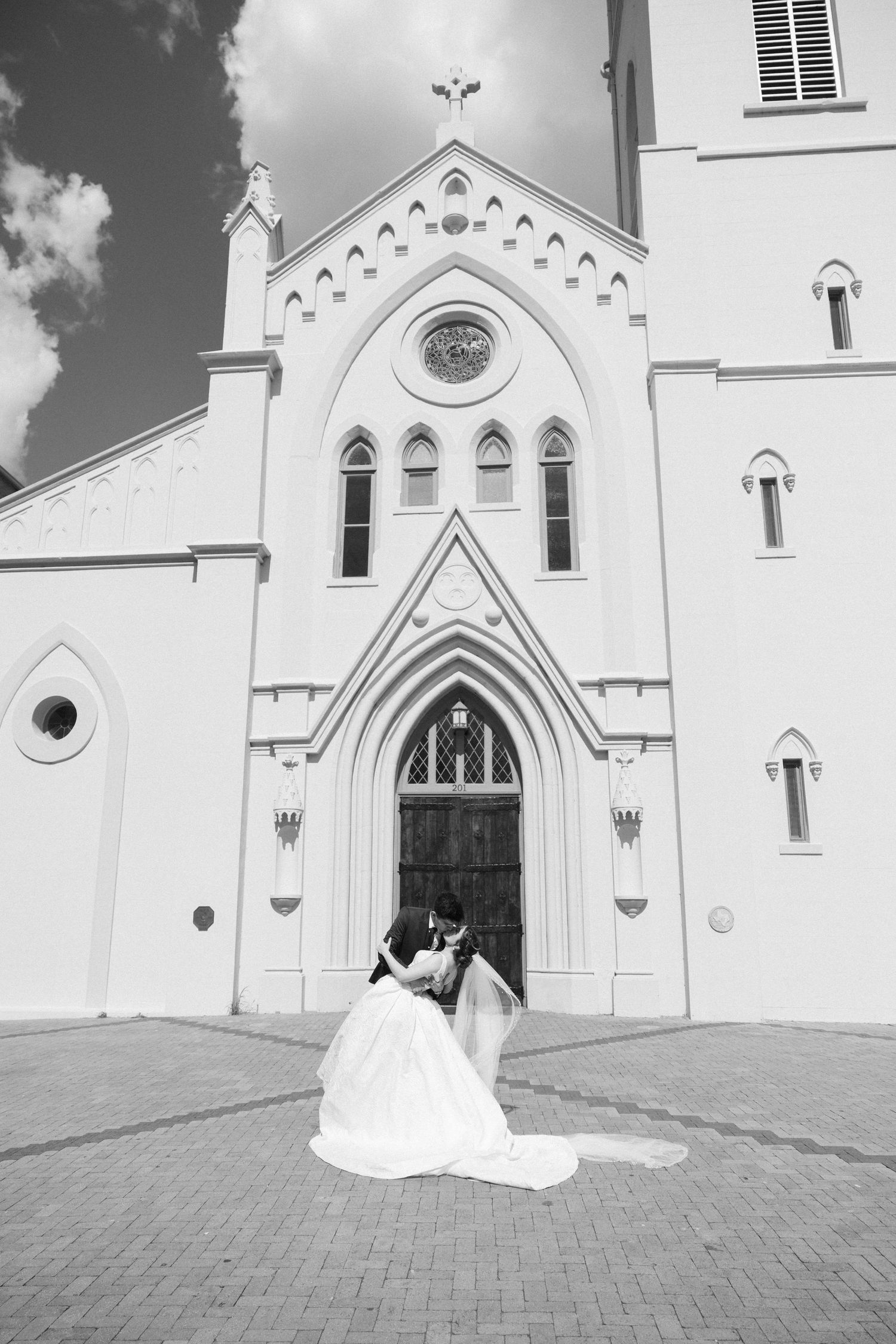 White church exterior with Gothic architecture features and arched doorways on a sunny day.