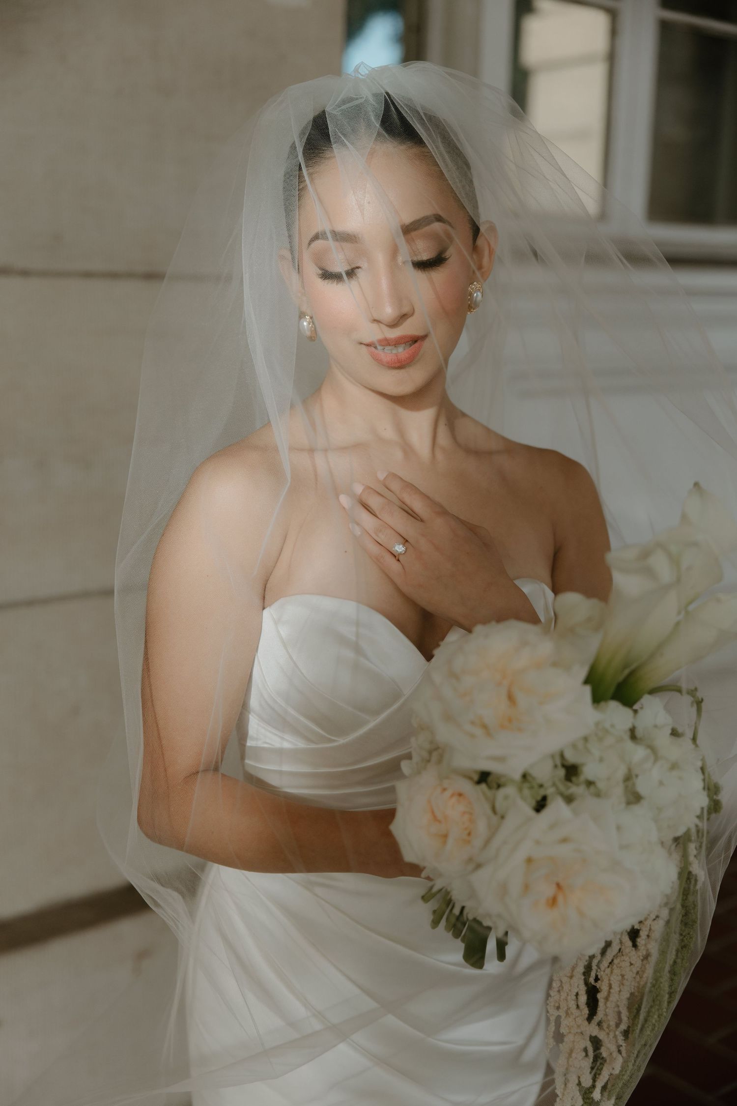 Bride in white dress holds bouquet of light-colored flowers.